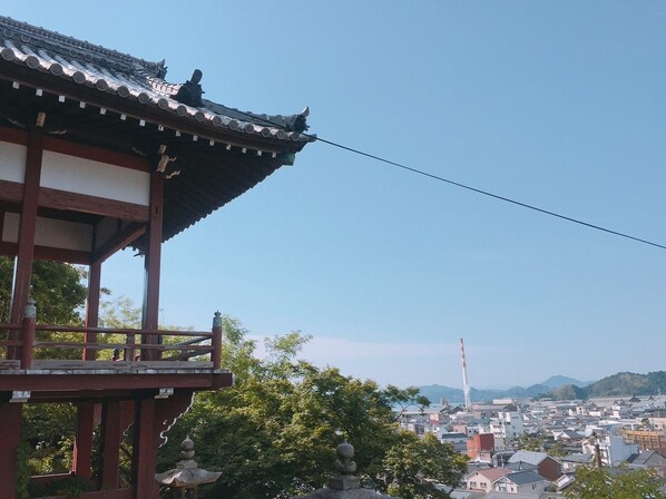 Un bâtiment japonais traditionnel, avec un toit en tuiles et une structure en bois, qui offre une vue sur un paysage urbain dominé par une tour imposante.