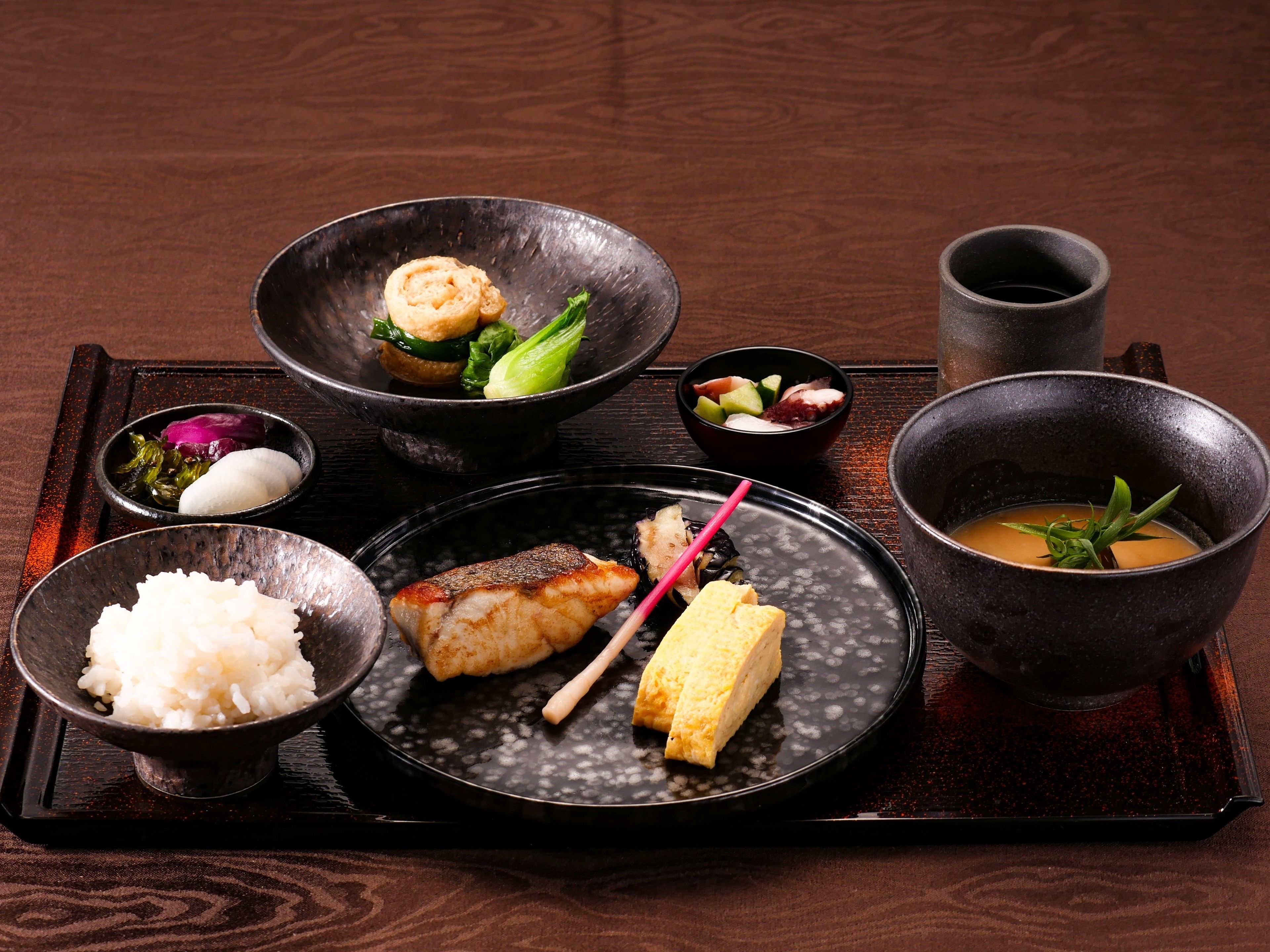 Una comida tradicional japonesa con arroz, pescado y sopa sobre una bandeja.