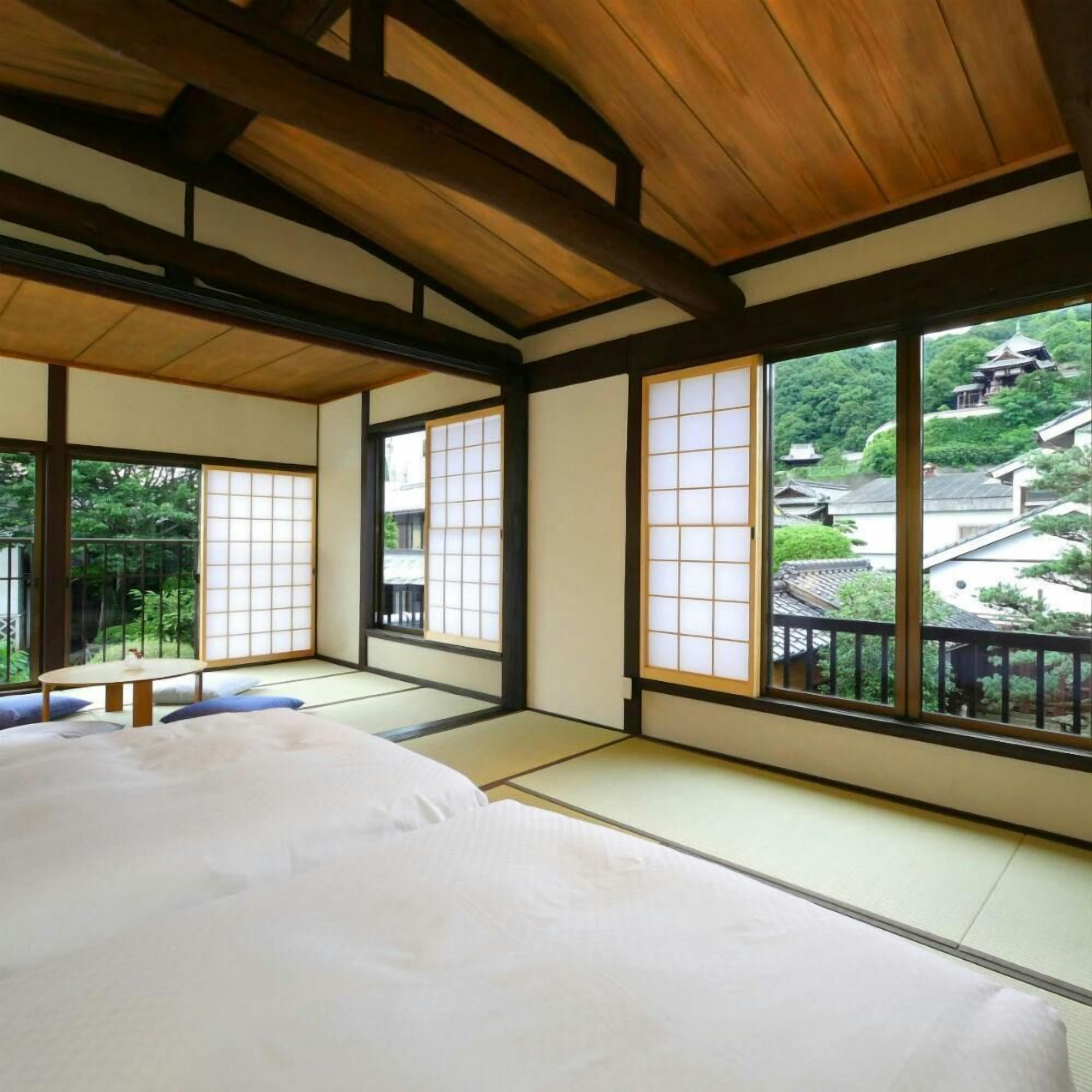 Um quarto japonês tradicional com tatames, teto de madeira baixo e grandes portas deslizantes com vista para uma aldeia tradicional.