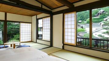 Um quarto japonês tradicional com tatames, teto de madeira baixo e grandes portas deslizantes com vista para uma aldeia tradicional.