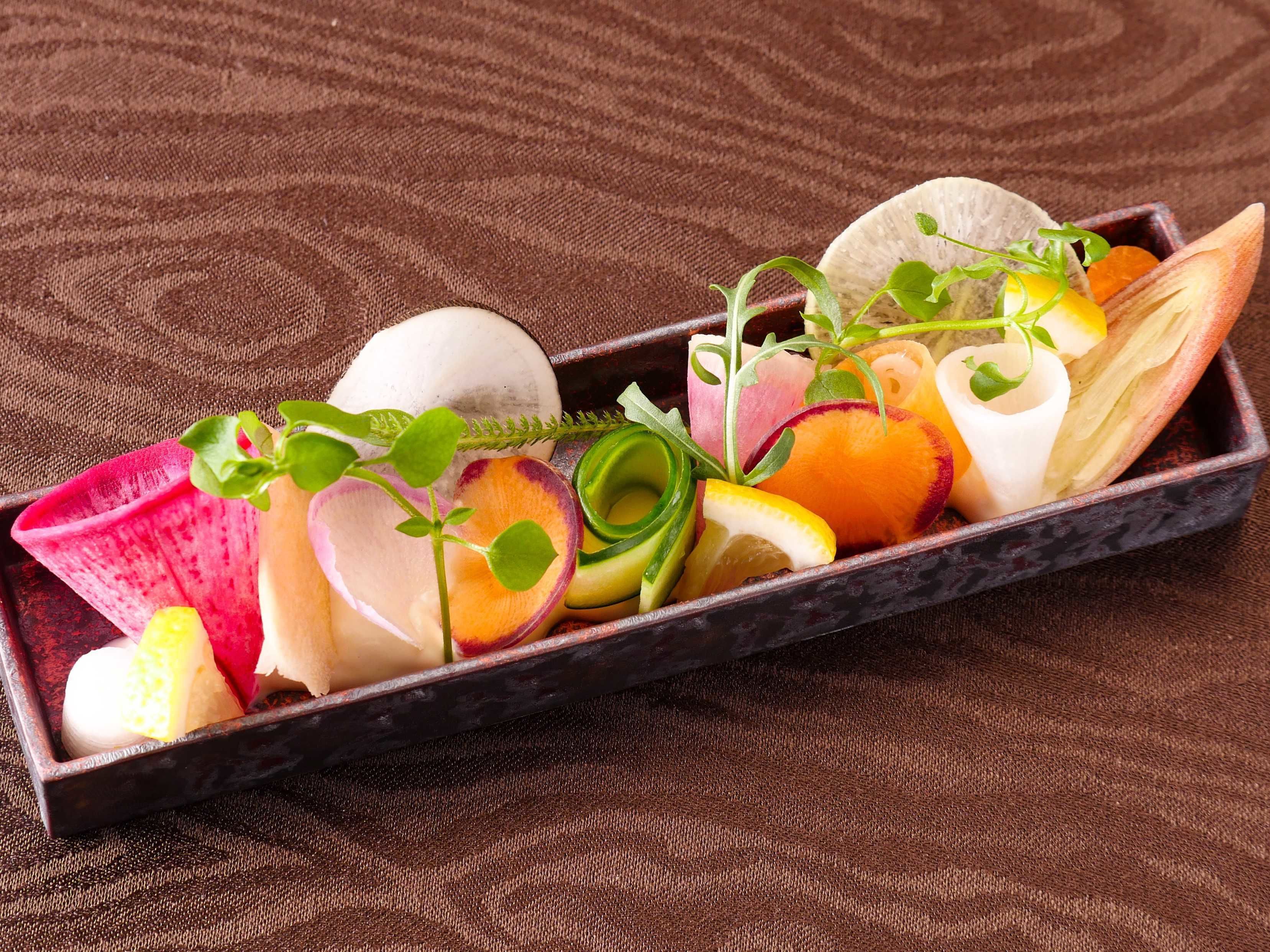 A wooden tray with various fruits and vegetables, including radishes, apples, and citrus slices, arranged on a textured brown surface.