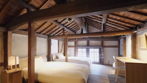 A rustic bedroom with wooden beams, two beds, a desk, and a chair.