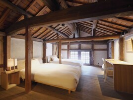 Un dormitorio rústico con vigas de madera, dos camas, un escritorio y una silla.