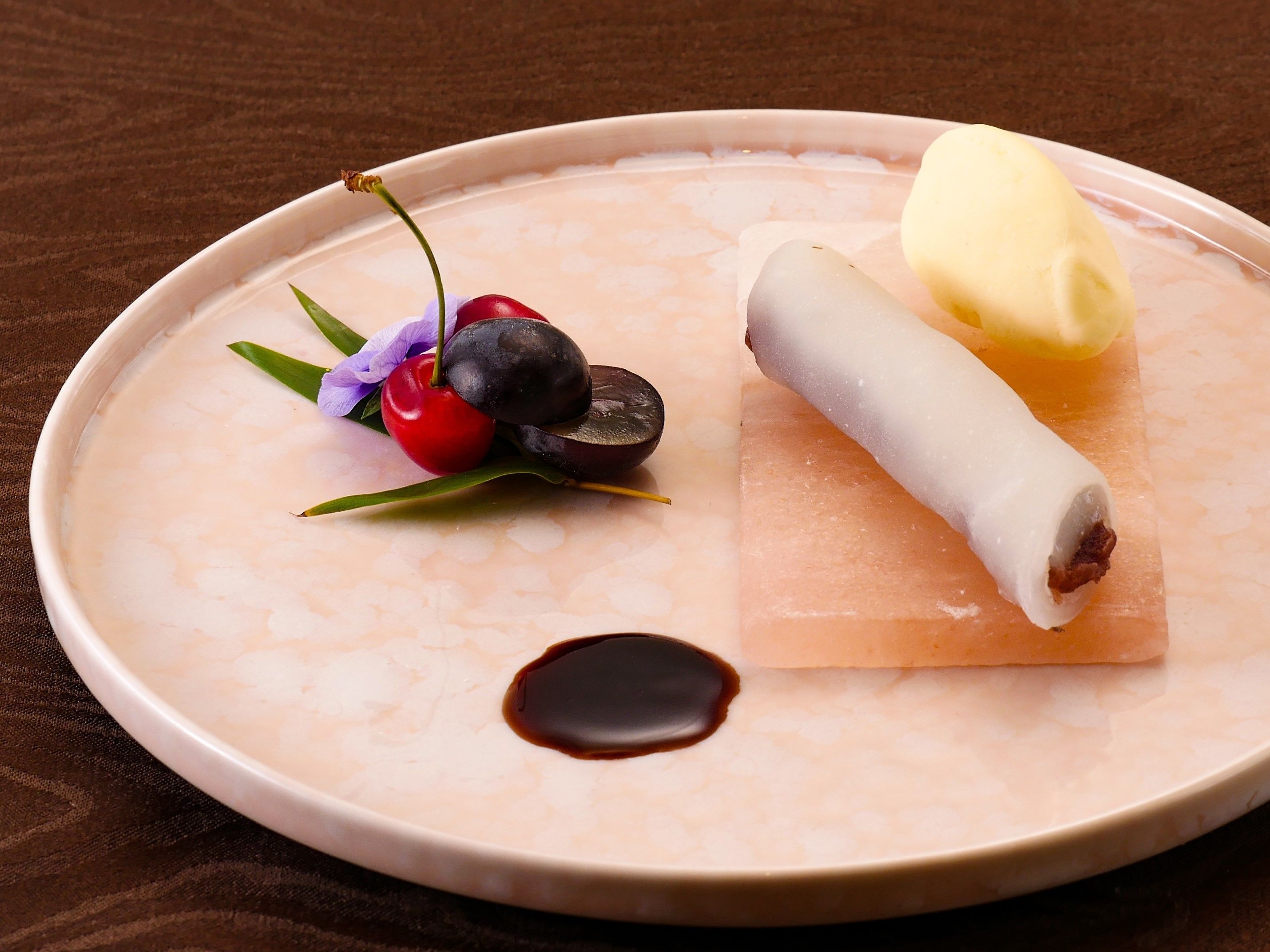 Un plato de postre con un pastel enrollado, una bola de helado y una cereza como decoración.