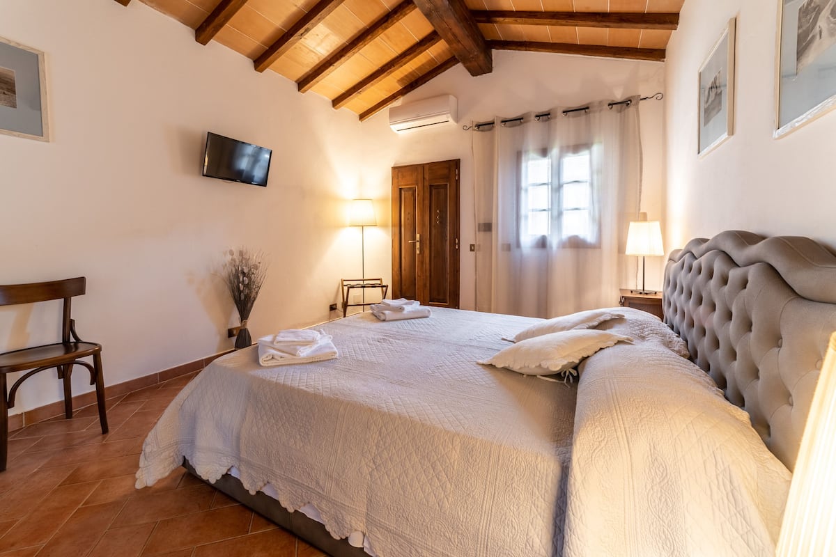 Un dormitorio con una cama grande, vigas de madera en el techo, un televisor de pantalla plana y una puerta que da a otra habitación.