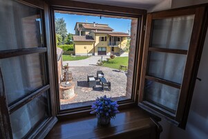 Vista desde una ventana de una casa con un patio, un camino de piedra y mobiliario exterior.