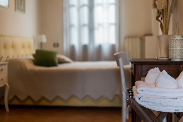 A neatly made bed with a green pillow, a chair with towels, and a bedside table with a vase. - Borgo Terrosi (Sinalunga)