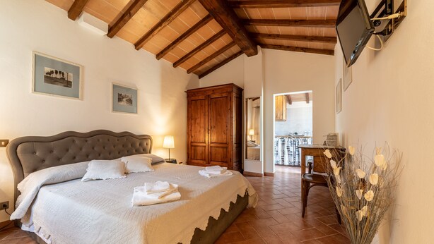 A bedroom with a large bed, wooden wardrobe, and a television mounted on the wall. - Borgo Terrosi (Sinalunga)