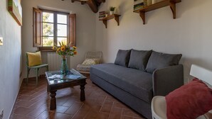 A cozy living room with a sofa, a chair, a coffee table, and a window with open shutters. - Borgo Terrosi (Sinalunga)