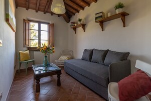 Una sala de estar acogedora con un sofá, un sillón, una mesa de centro y una ventana con contraventanas abiertas.