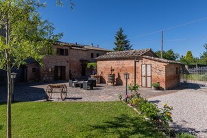 Una casa de ladrillo rústica con un patio, mobiliario exterior y un carruaje tirado por caballos.