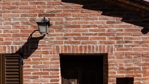 A rustic brick building with a wooden door, a small window with shutters, and a lantern on the wall. - Borgo Terrosi (Sinalunga)