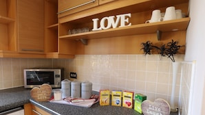 A kitchen with wooden cabinets, a microwave, and a countertop with various items including jars labeled 'SUGAR' and 'TEA'. - O2 Mailbox Central Premier Apartment (Birmingham)