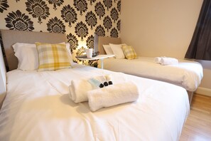A hotel room with two beds, each with white linens and a rolled towel. There is a small table with a laptop and a cup. - O2 Mailbox Central Premier Apartment (Birmingham)
