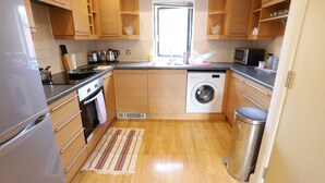 A compact kitchen with wooden cabinets, a washing machine, and a microwave. - O2 Mailbox Central Premier Apartment (Birmingham)