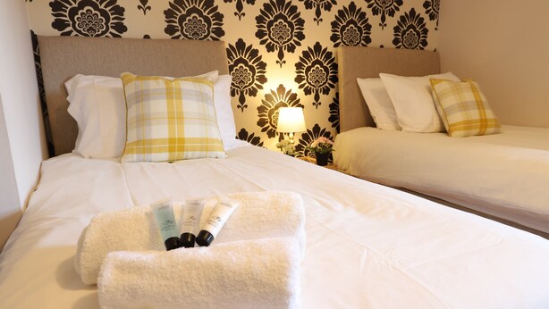 A hotel room with a neatly made bed, a bedside table with a lamp, and a wall with a floral pattern. - O2 Mailbox Central Premier Apartment (Birmingham)