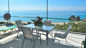Ein Glastisch mit Stühlen und einem Blumentopf auf einem Balkon mit Blick auf Strand und Meer.