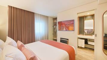 A hotel room with a large bed, a shower area, a vanity with a mirror, and a framed picture on the wall.