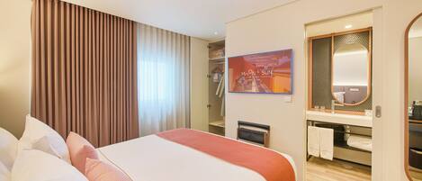 A hotel room with a large bed, a shower area, a vanity with a mirror, and a framed picture on the wall.