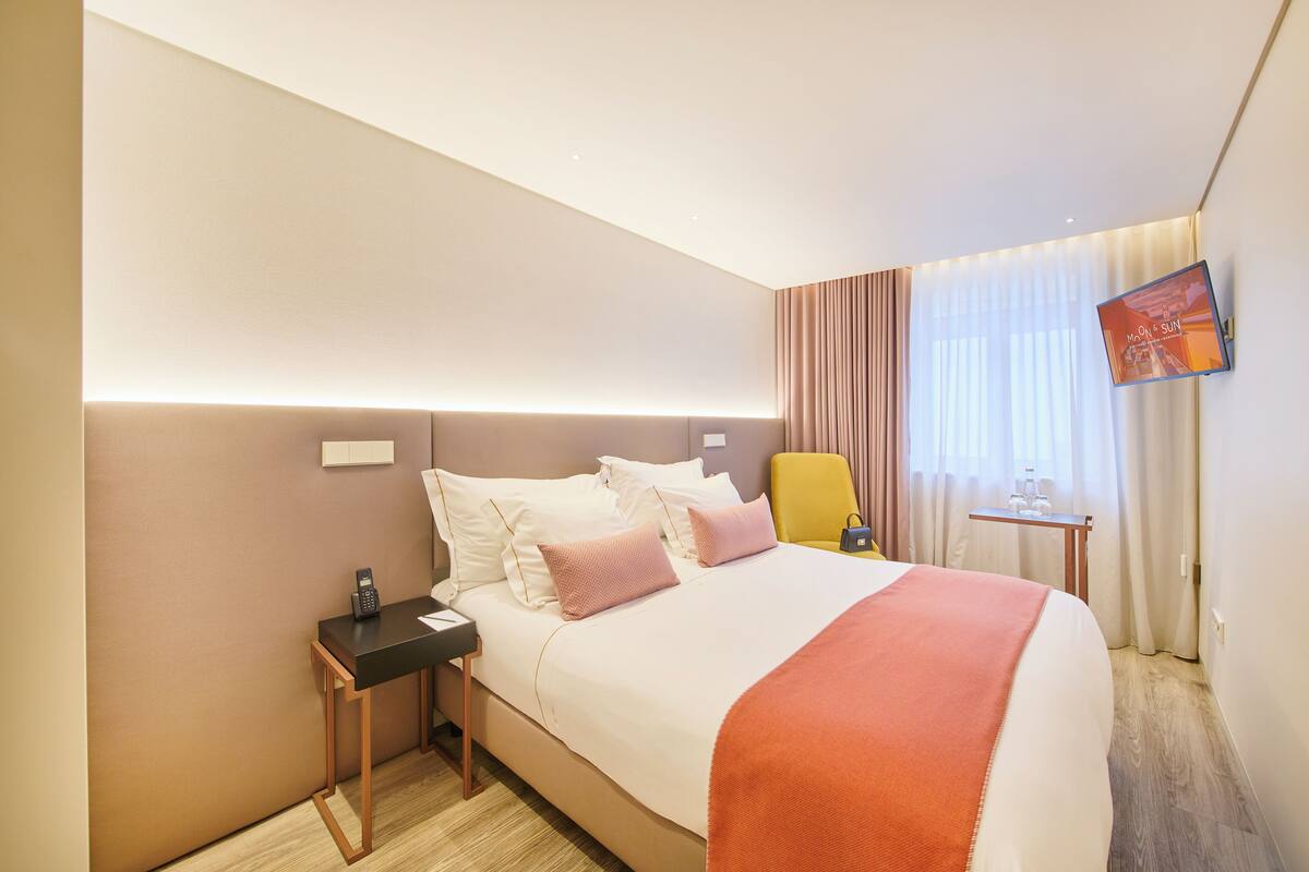 Ein Hotelzimmer mit Bett, Nachttisch, Sessel, Fernseher und Vorhängen.