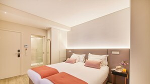 Een moderne hotelkamer met een groot bed, een nachtkastje met een boek en een glas sinaasappelsap, en een deur met een digitaal slot.