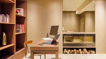 A modern room with a wooden desk, a laptop, a chair, a bookshelf, and a fireplace.