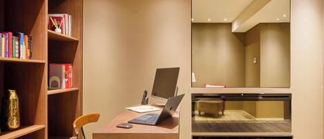 A modern room with a wooden desk, a laptop, a chair, a bookshelf, and a fireplace.