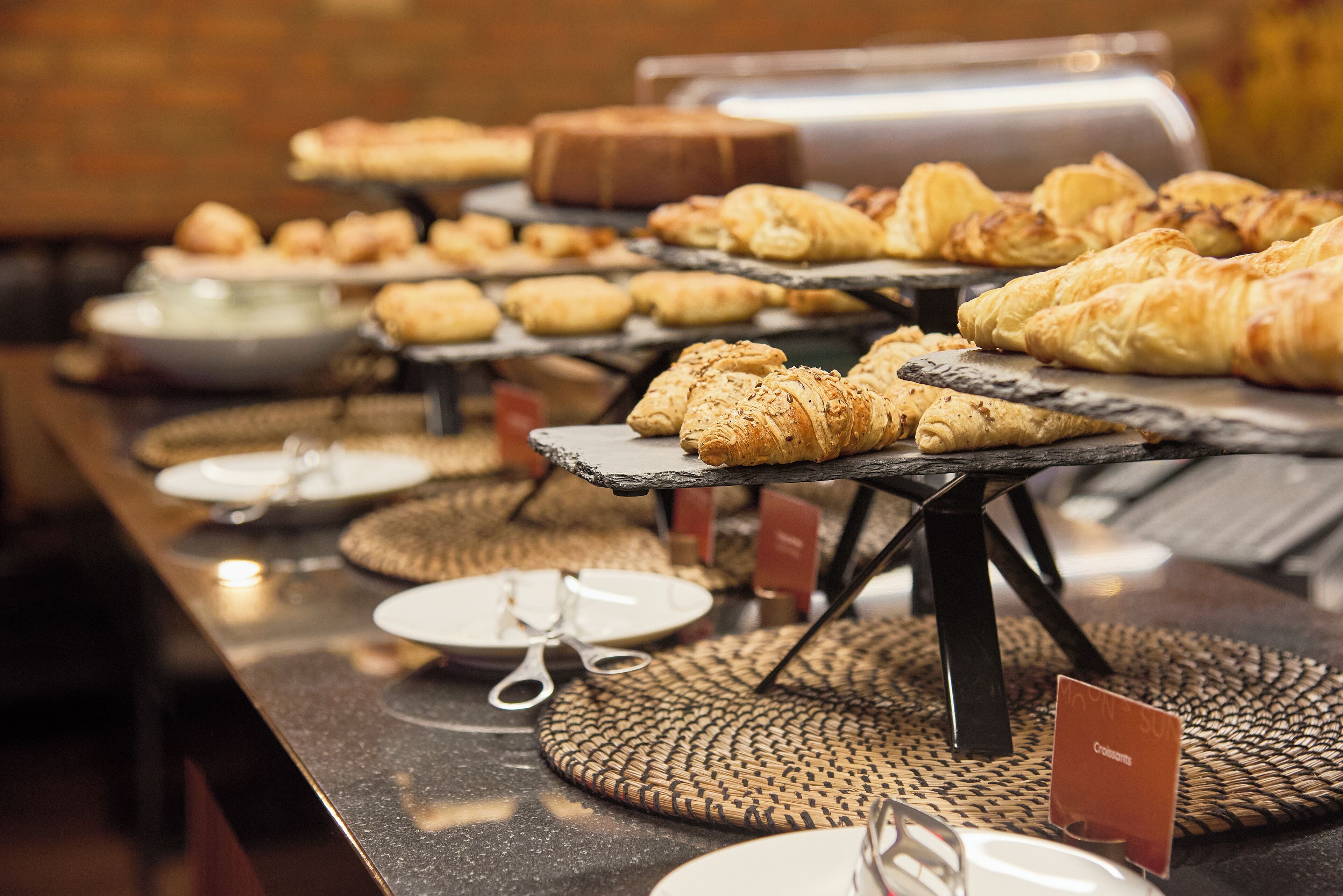 Un buffet proposant une variété de viennoiseries et de pains, présentés sur des présentoirs en ardoise noire.