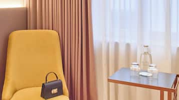 Hotelkamer met een geel fauteuil, een kleine tafel met fles en glazen, en een paar schoenen op de vloer.