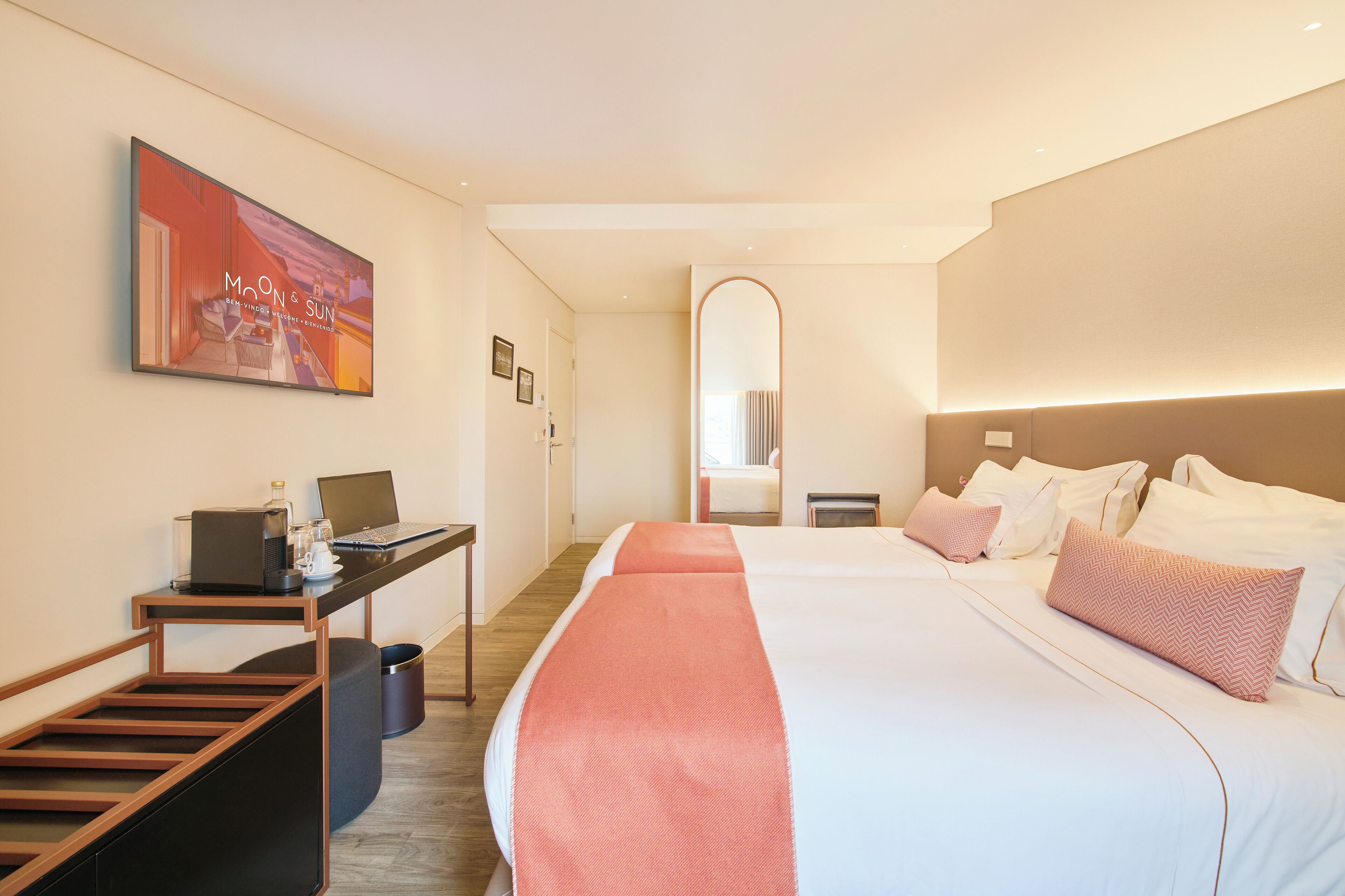 A hotel room with a bed, a desk with a laptop, a chair, and a trash bin.