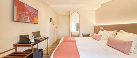 A hotel room with a bed, a desk with a laptop, a chair, and a trash bin.