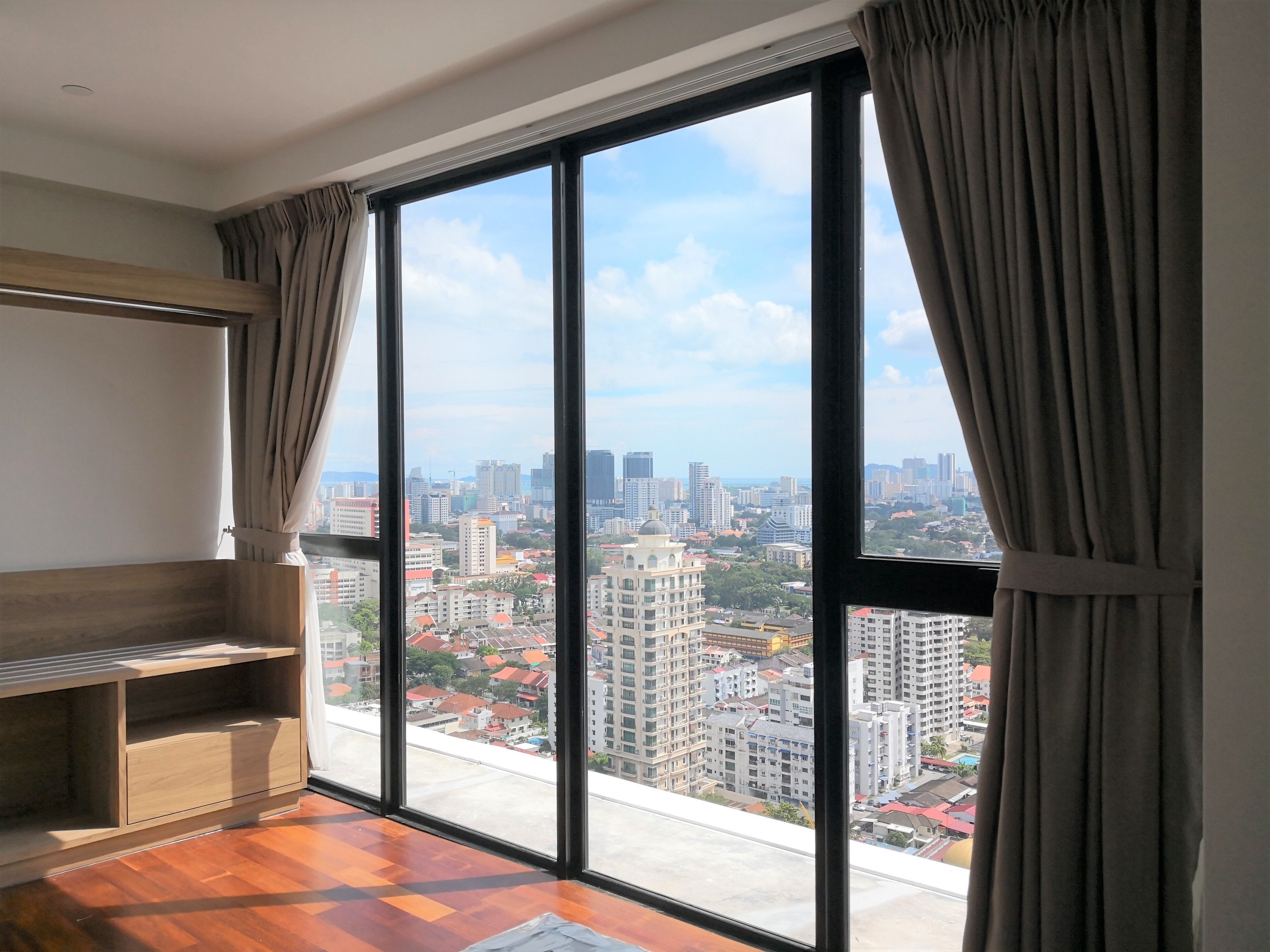 A room with a large window, a wooden cabinet, and a view of a cityscape.