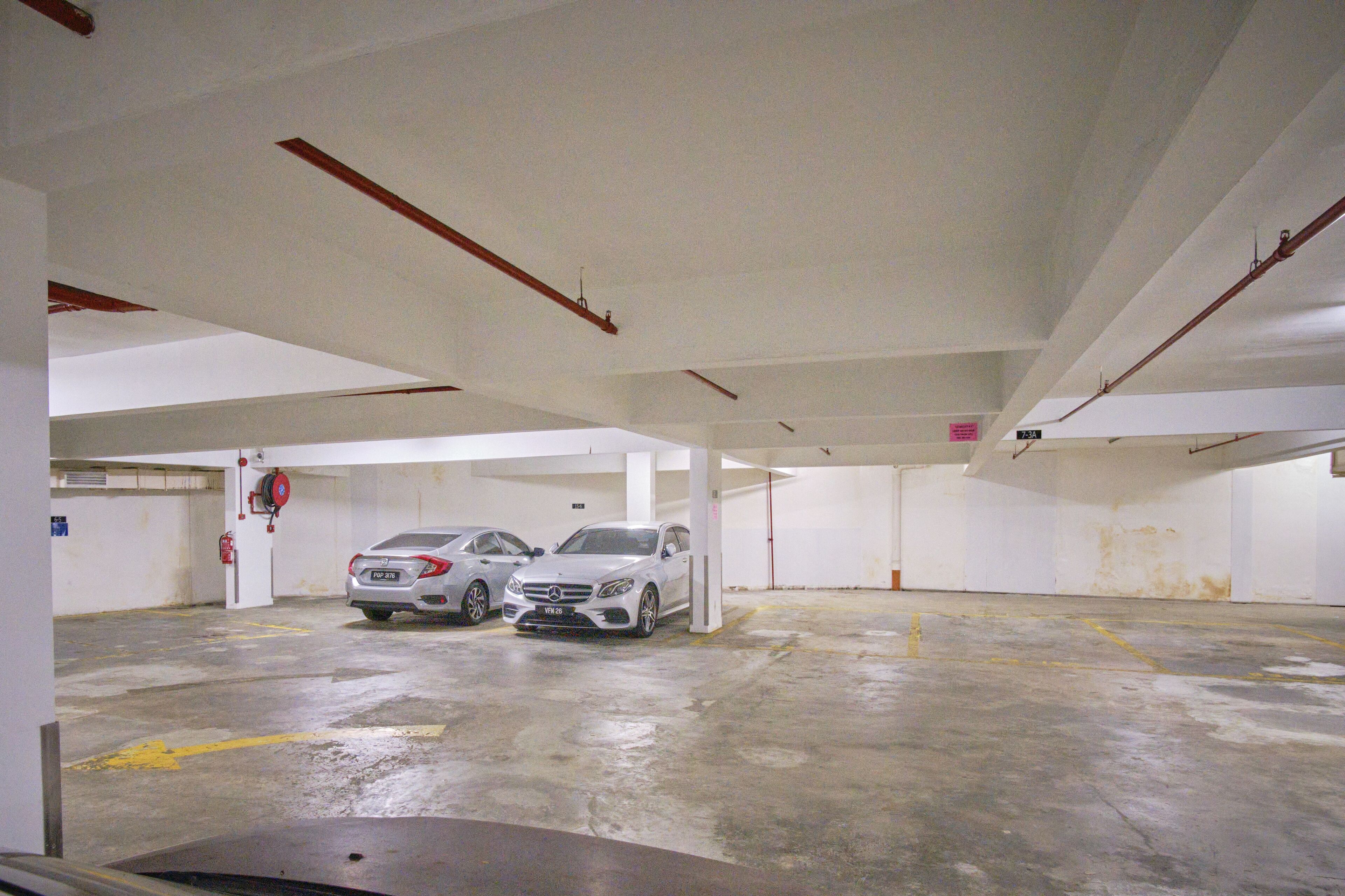 Garagem de estacionamento com dois carros, pisos de concreto, paredes brancas e vigas estruturais visíveis.