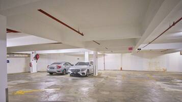 Garagem de estacionamento com dois carros, pisos de concreto, paredes brancas e vigas estruturais visíveis.