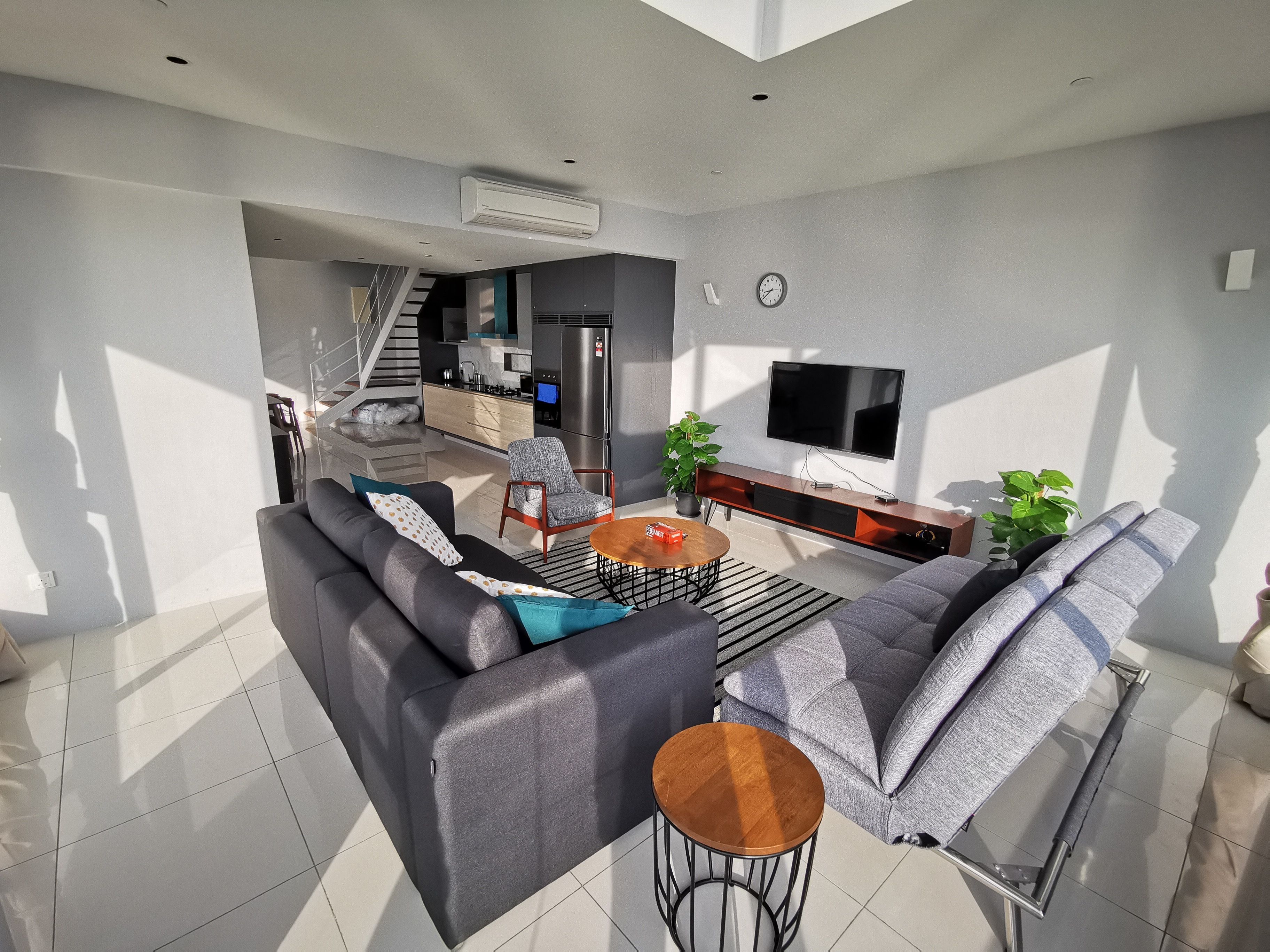 A modern living room with a sofa, a coffee table, and a TV. There is a staircase leading to an upper level.