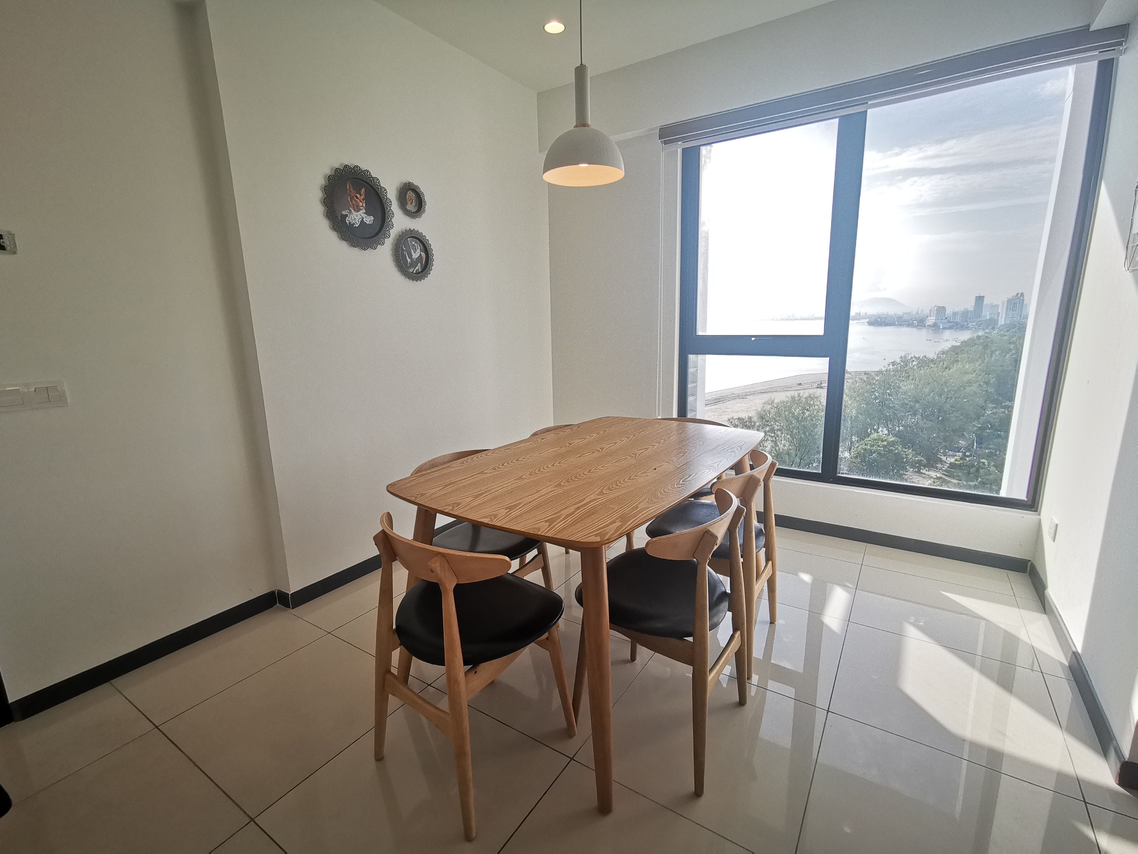 A dining area with a wooden table and chairs, a pendant light, and a large window with a view of a cityscape.
