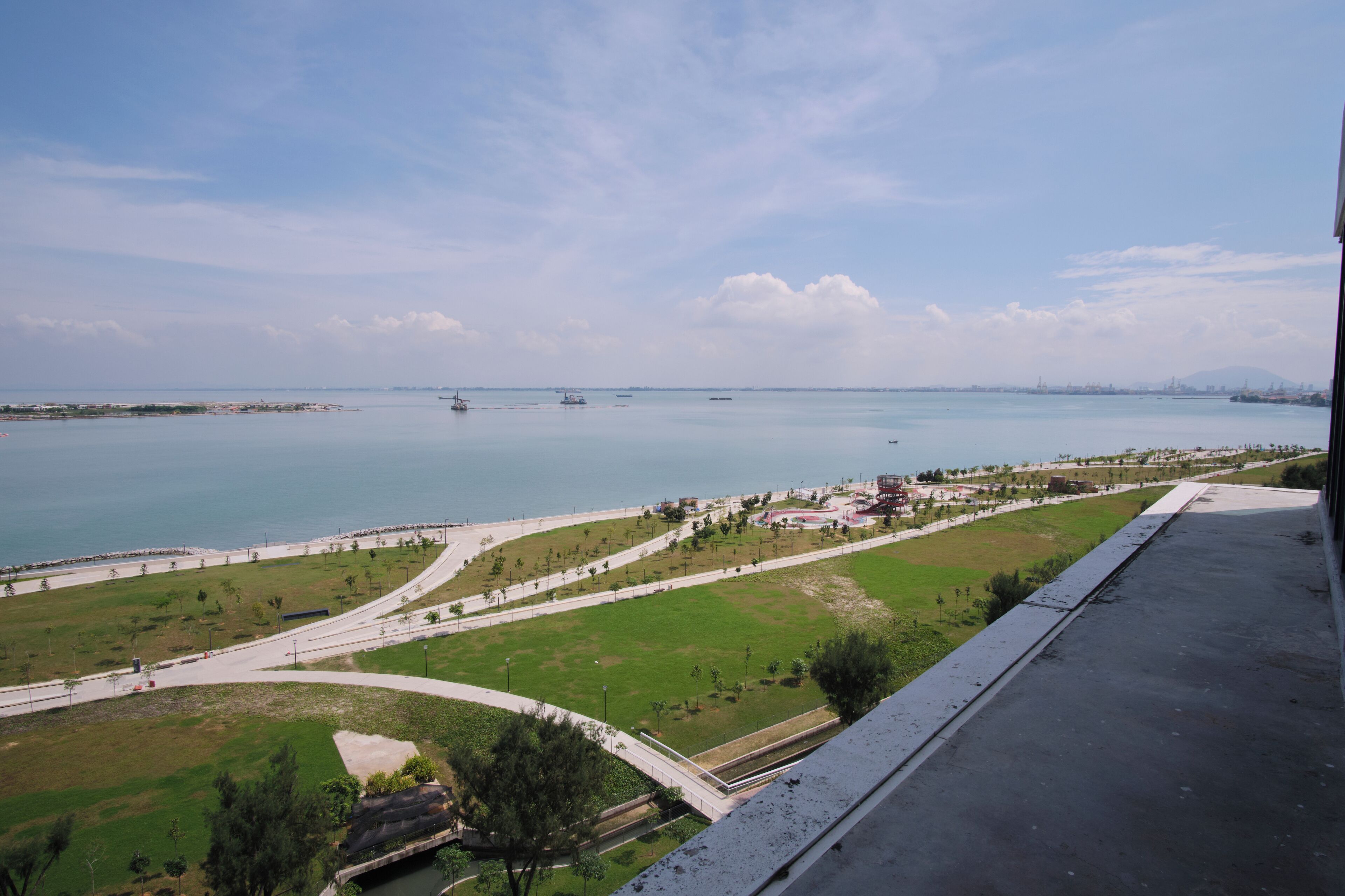 A coastal view with a promenade, a marina, and distant buildings.