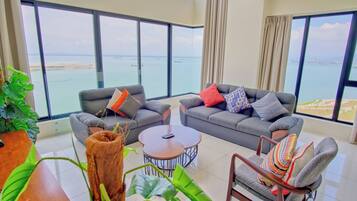 A modern living room with large windows, grey sofas, a wooden coffee table, and a striped armchair.