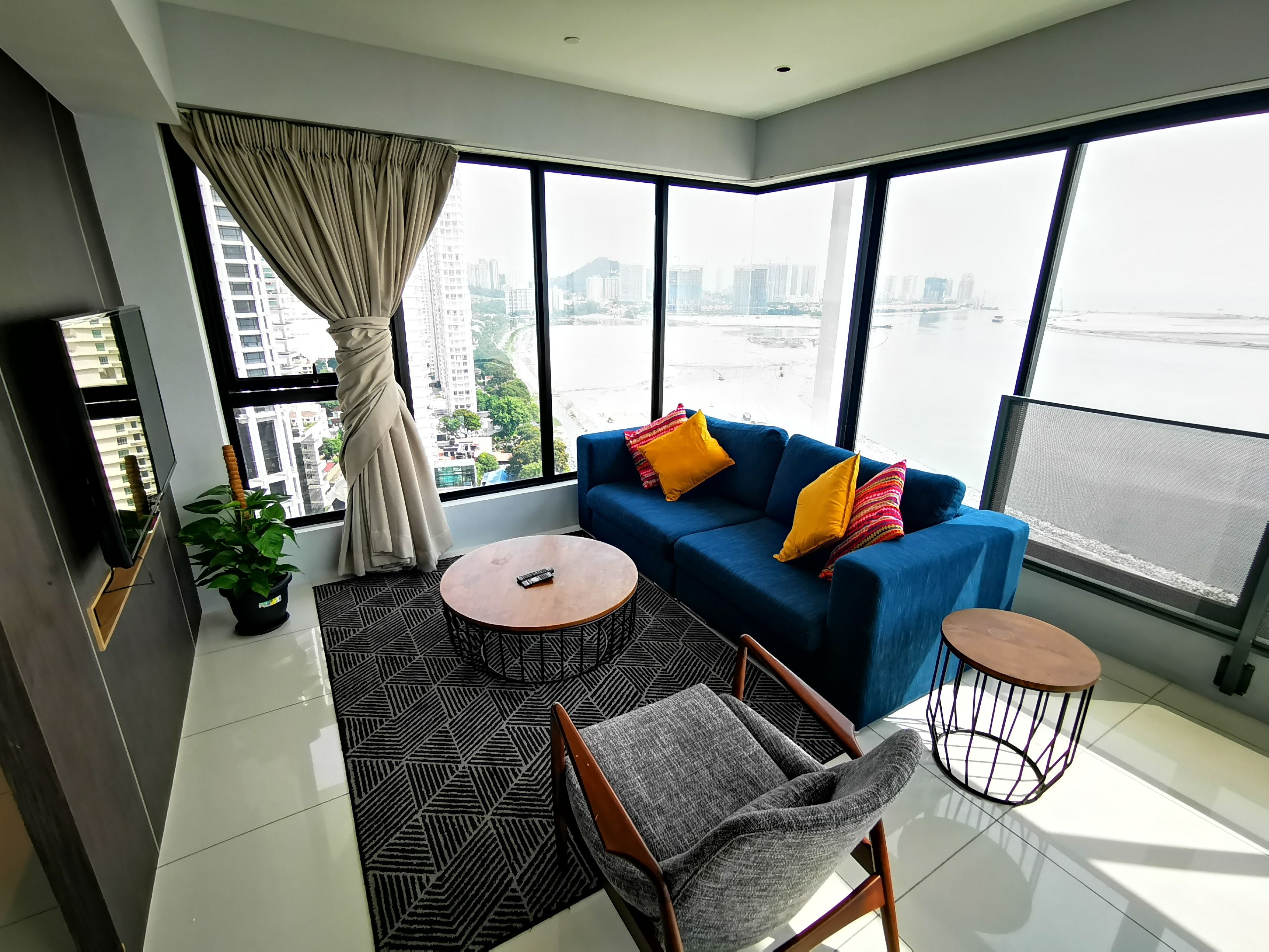 Una sala de estar moderna con un sofá, dos mesitas auxiliares, un sillón, un ventanal con vistas a la ciudad y una planta en maceta.