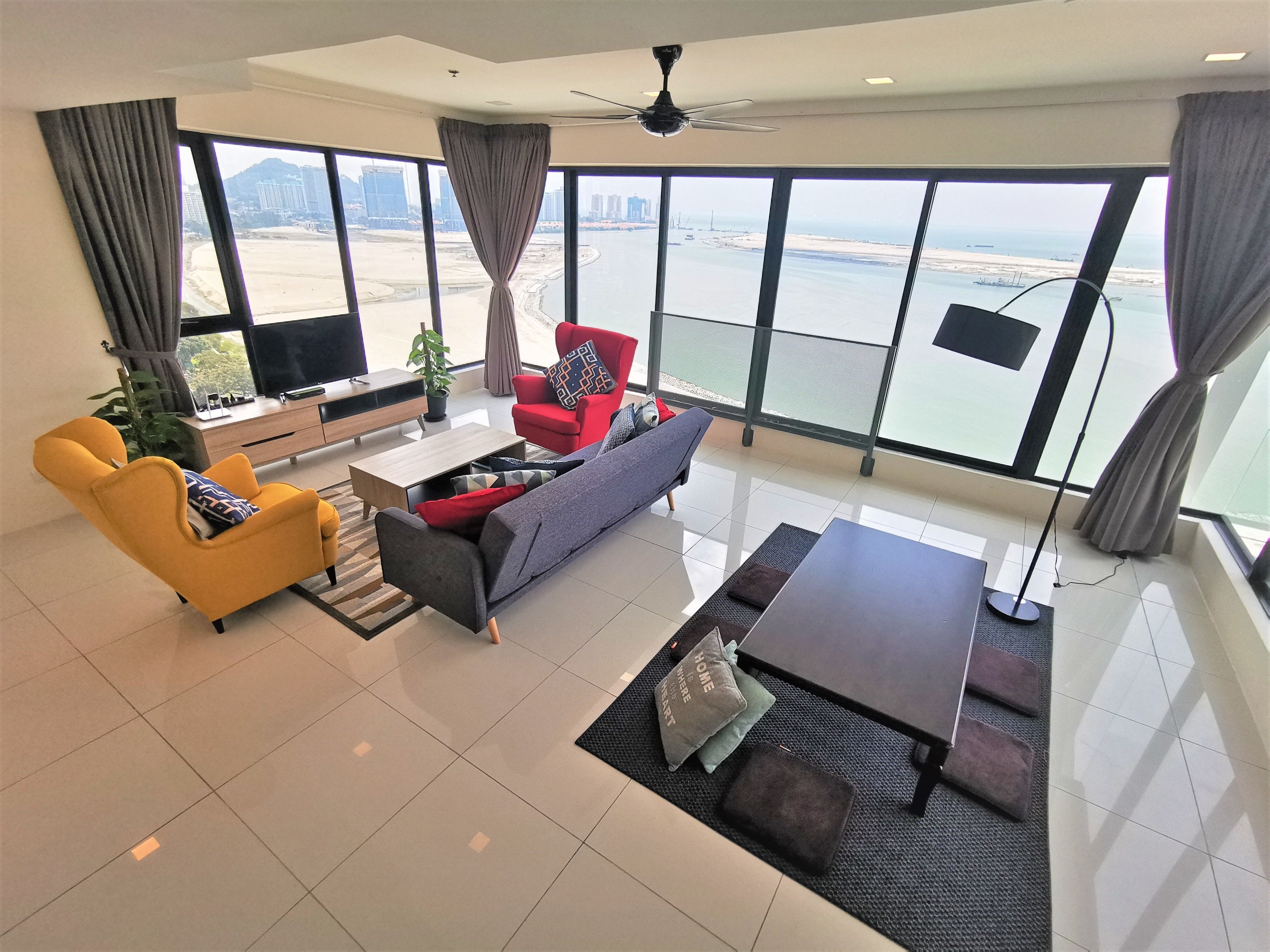 A modern living room with a large window offering a view of a beach and cityscape.