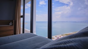 A bedroom with a large window overlooking a body of water and a distant shoreline. - Family Suite Sunrise Gurney Penang (George Town)
