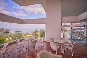 Een balkon met rieten meubels, een zwembad en uitzicht op zee.