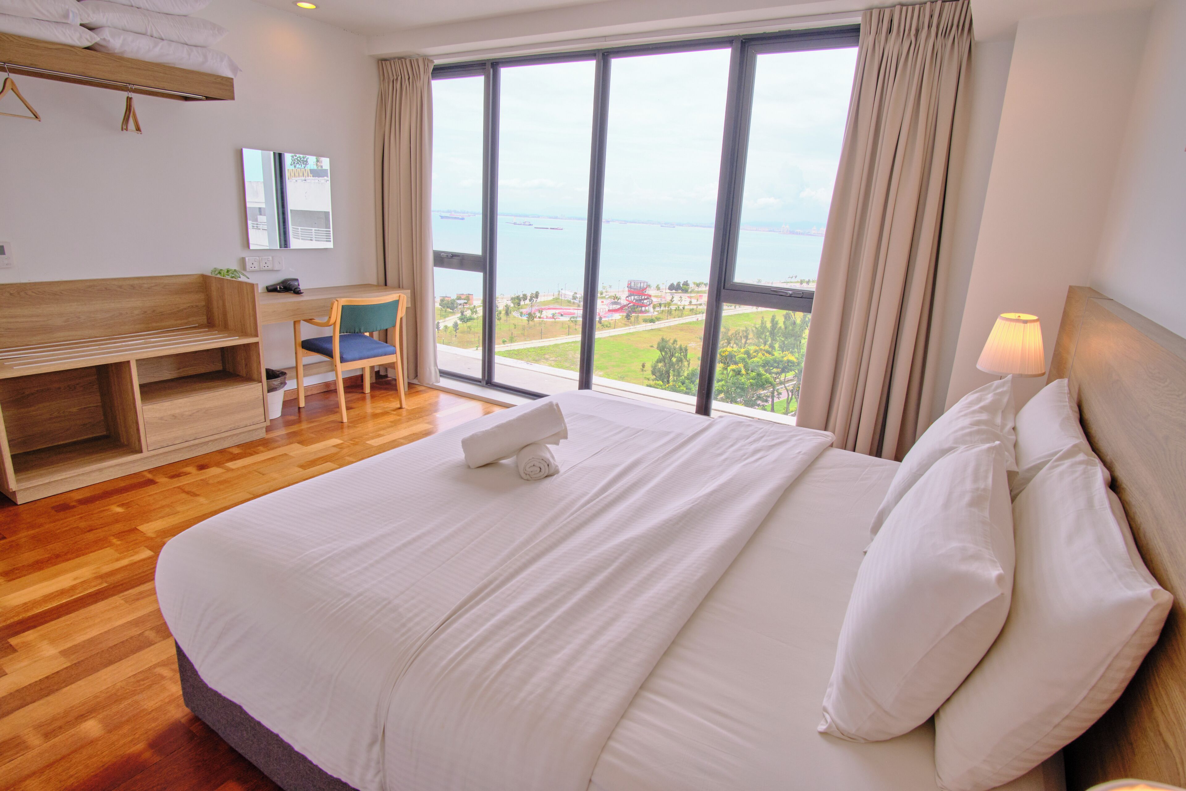 A hotel room with a large bed, a desk, a chair, and a view of the sea.