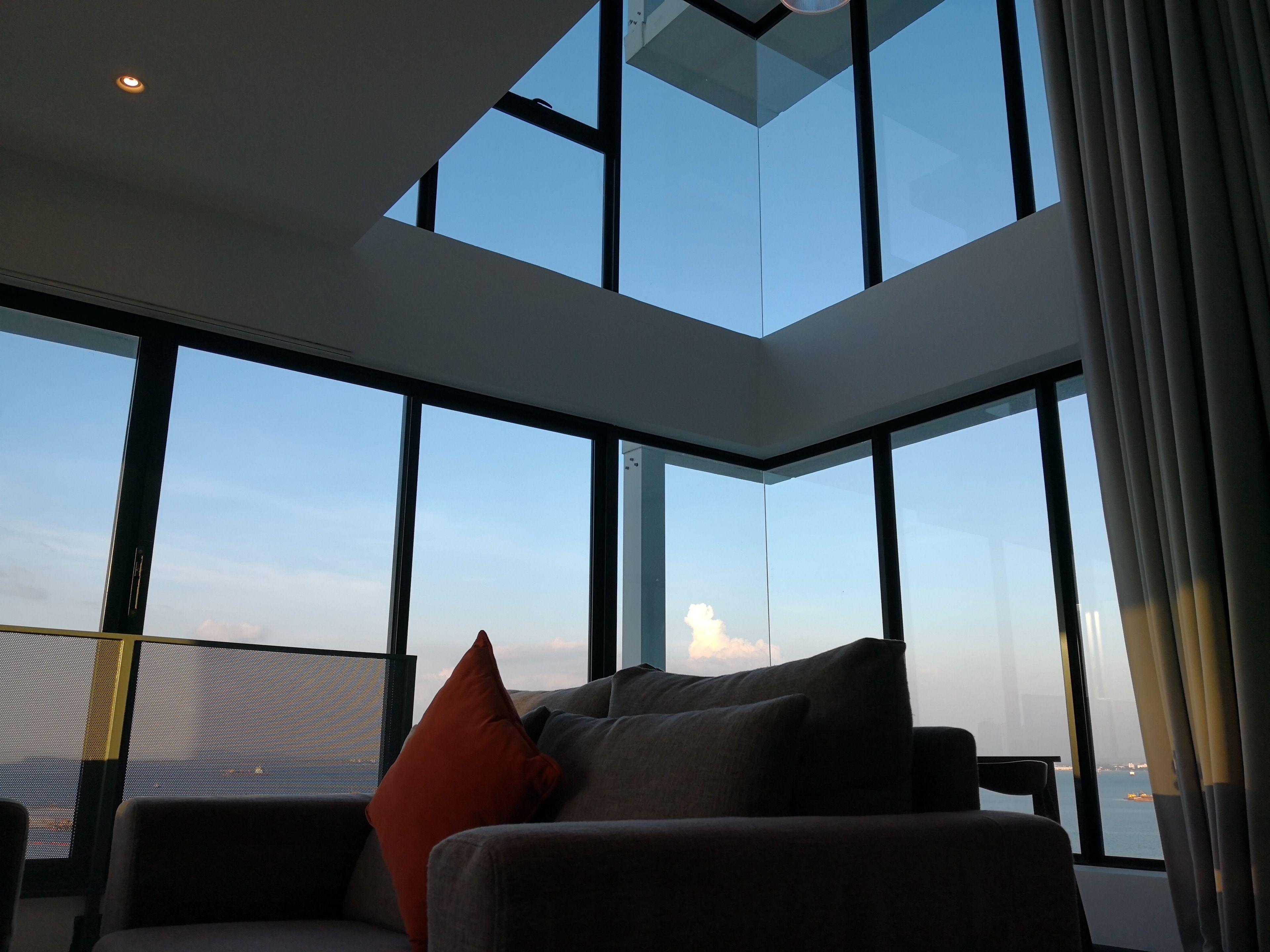 Ein modernes Zimmer mit großen Fenstern, einer Couch und Blick zum Himmel.