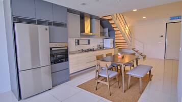 A modern kitchen with a built-in oven, microwave, and refrigerator. There is a dining area with a table and chairs, and a staircase leading to another level.