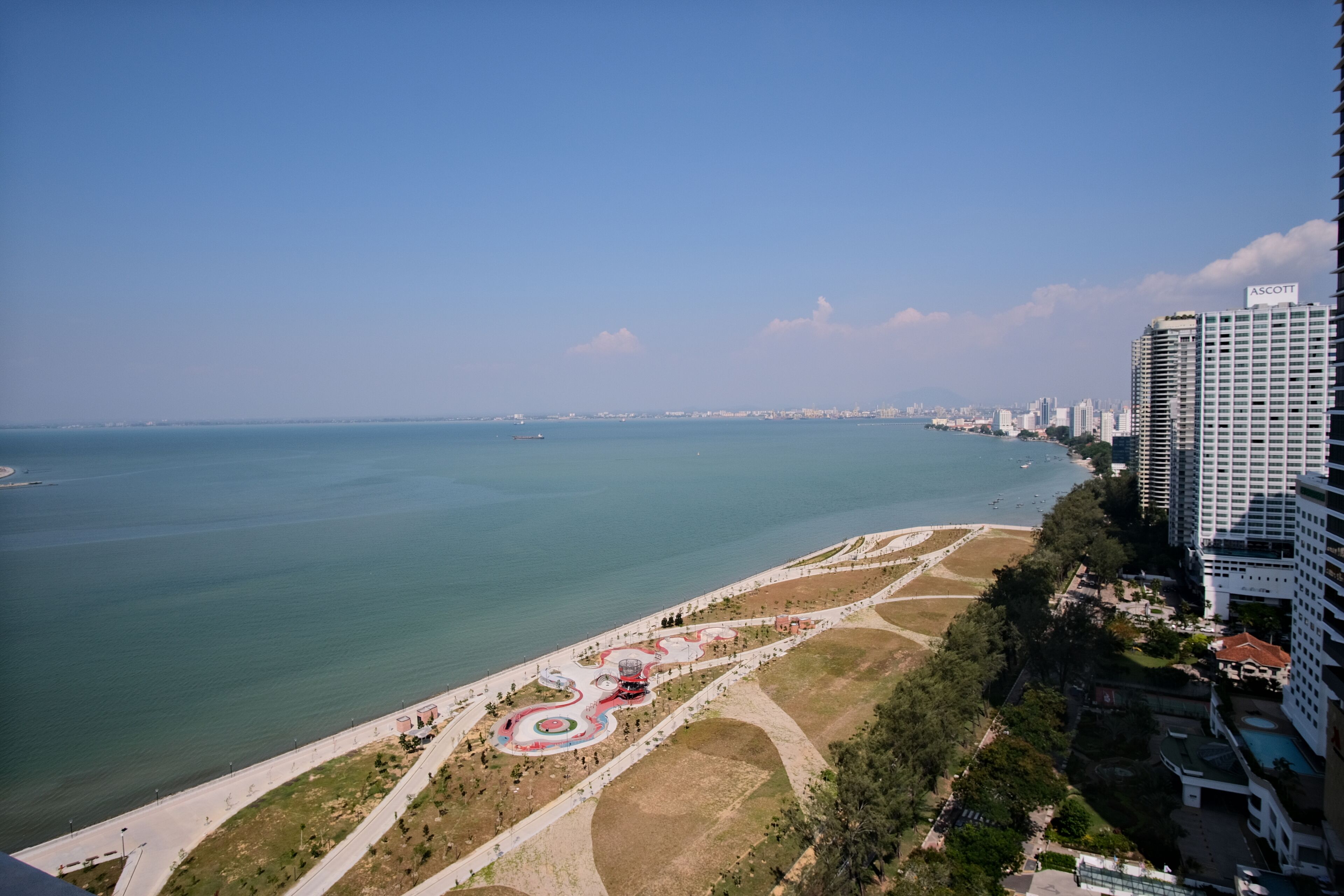 A coastal cityscape with a park featuring winding paths and a central circular area.