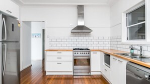 Uma cozinha moderna com armários brancos, fogão de aço inoxidável, forno embutido e lava-louças Bosch.