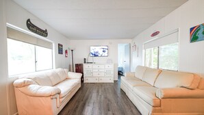 A spacious living room with two cream-colored sofas, a white cabinet, and a flat-screen TV on the wall. - Rainbow River Getaway (Dunnellon)