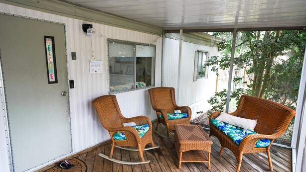 A covered porch with wicker furniture, including rocking chairs and a sofa, and a wooden floor. - Rainbow River Getaway (Dunnellon)