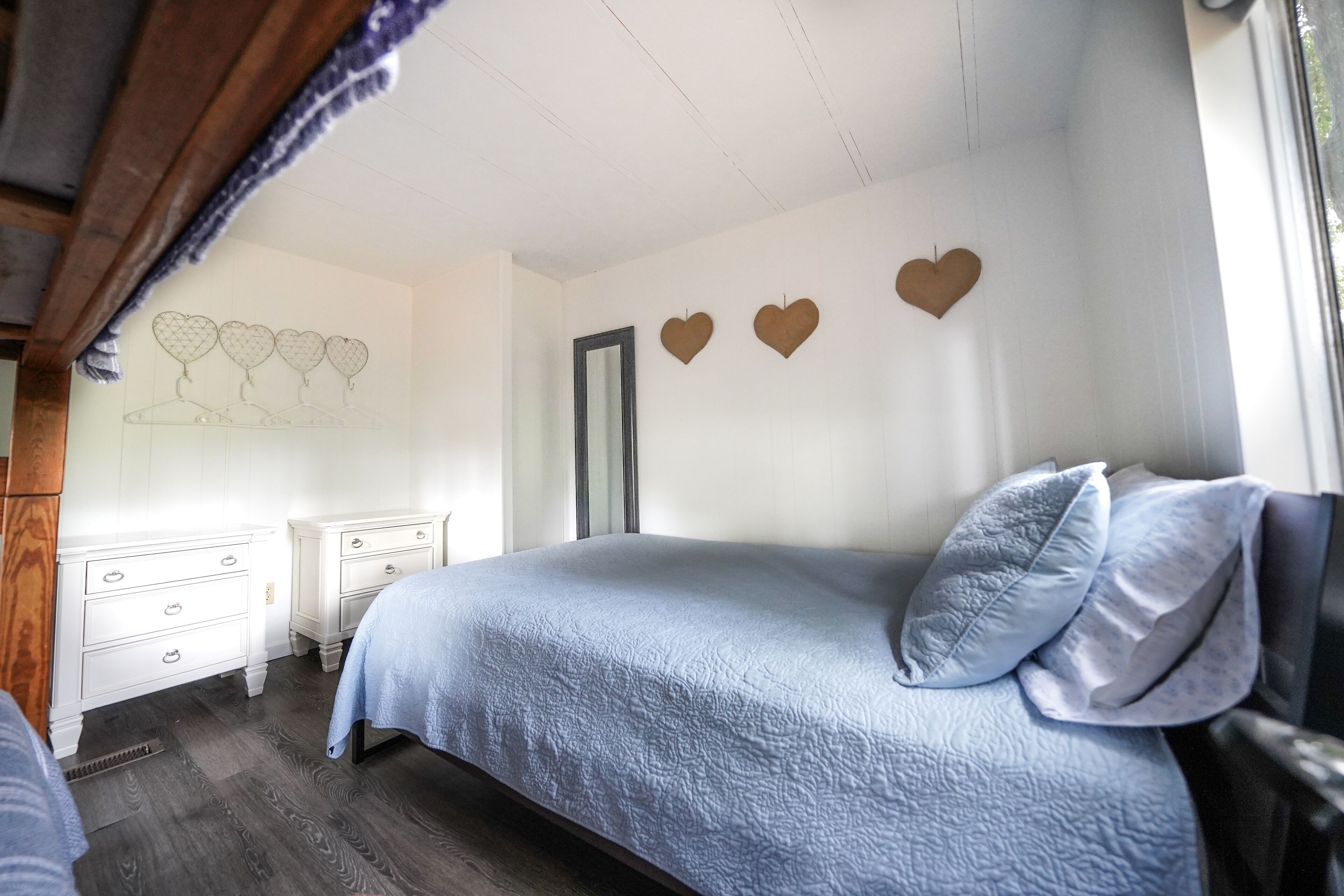A bedroom with a bed, two nightstands, a dresser, and a wall with heart-shaped decorations.